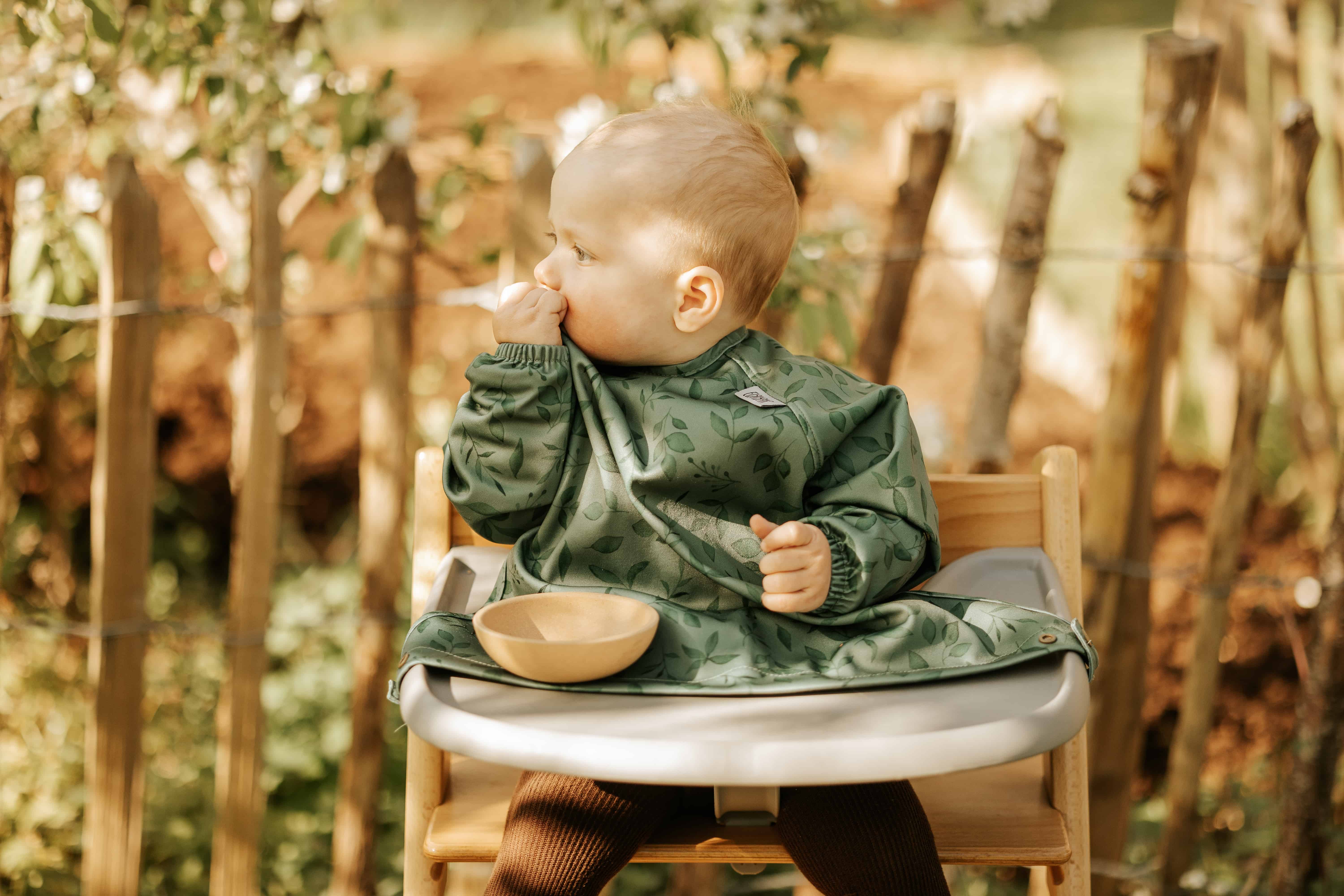 Baby spiser ved et bord med en langærmet hagesmæk på.